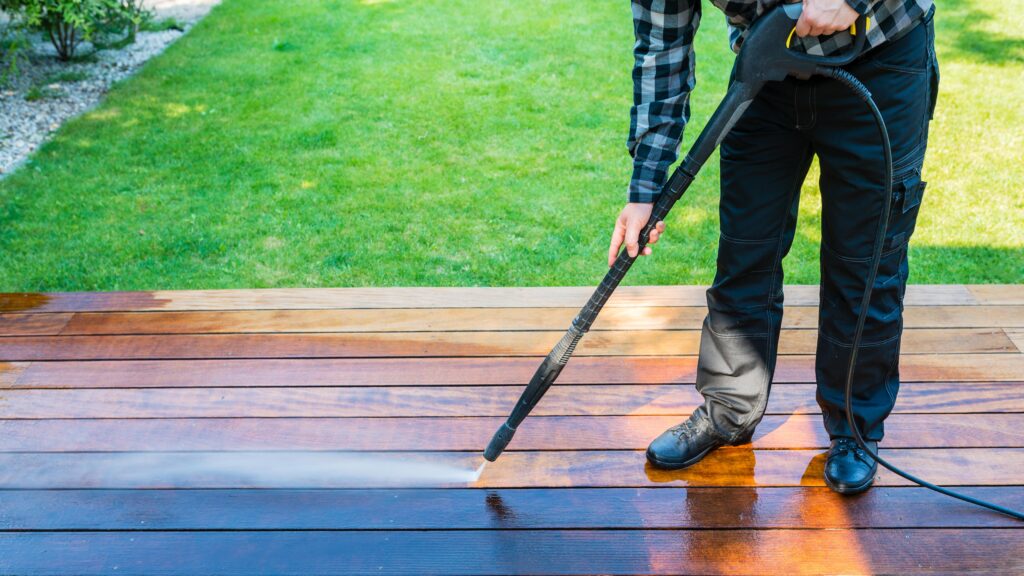 power washing - man cleaning terrace with a power washer - high water pressure cleaner on wooden terrace surface